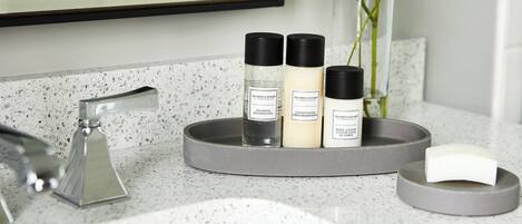 Un meuble-lavabo de salle de bain doté d’un robinet moderne, d’un porte-savon et de trois flacons de produits de soins pour la peau.