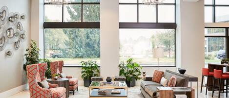 A spacious living room with large windows, modern furniture, and a chandelier.