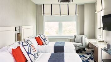 A hotel room with two beds, a desk, a chair, a TV, and a window with a city view.