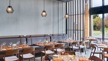 A restaurant with a modern interior, featuring wooden tables and chairs, and hanging pendant lights.