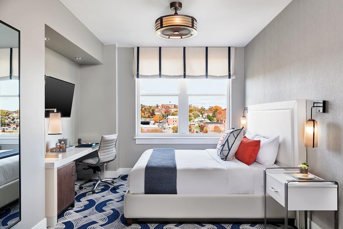 Habitación de hotel con cama, escritorio, silla y un ventanal que ofrece vistas a la ciudad.