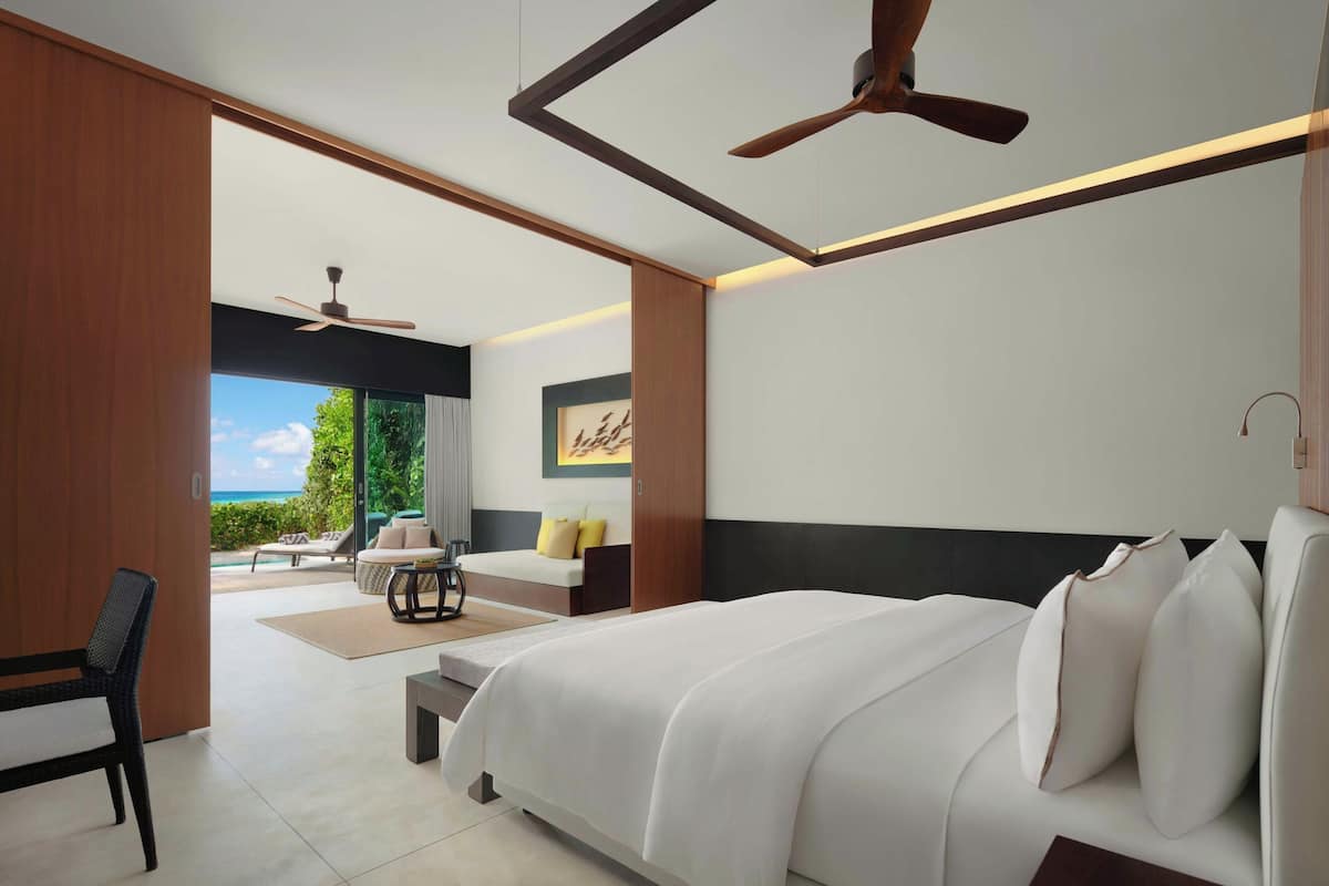 A modern bedroom with a large bed, a ceiling fan, and a view of the outdoors.