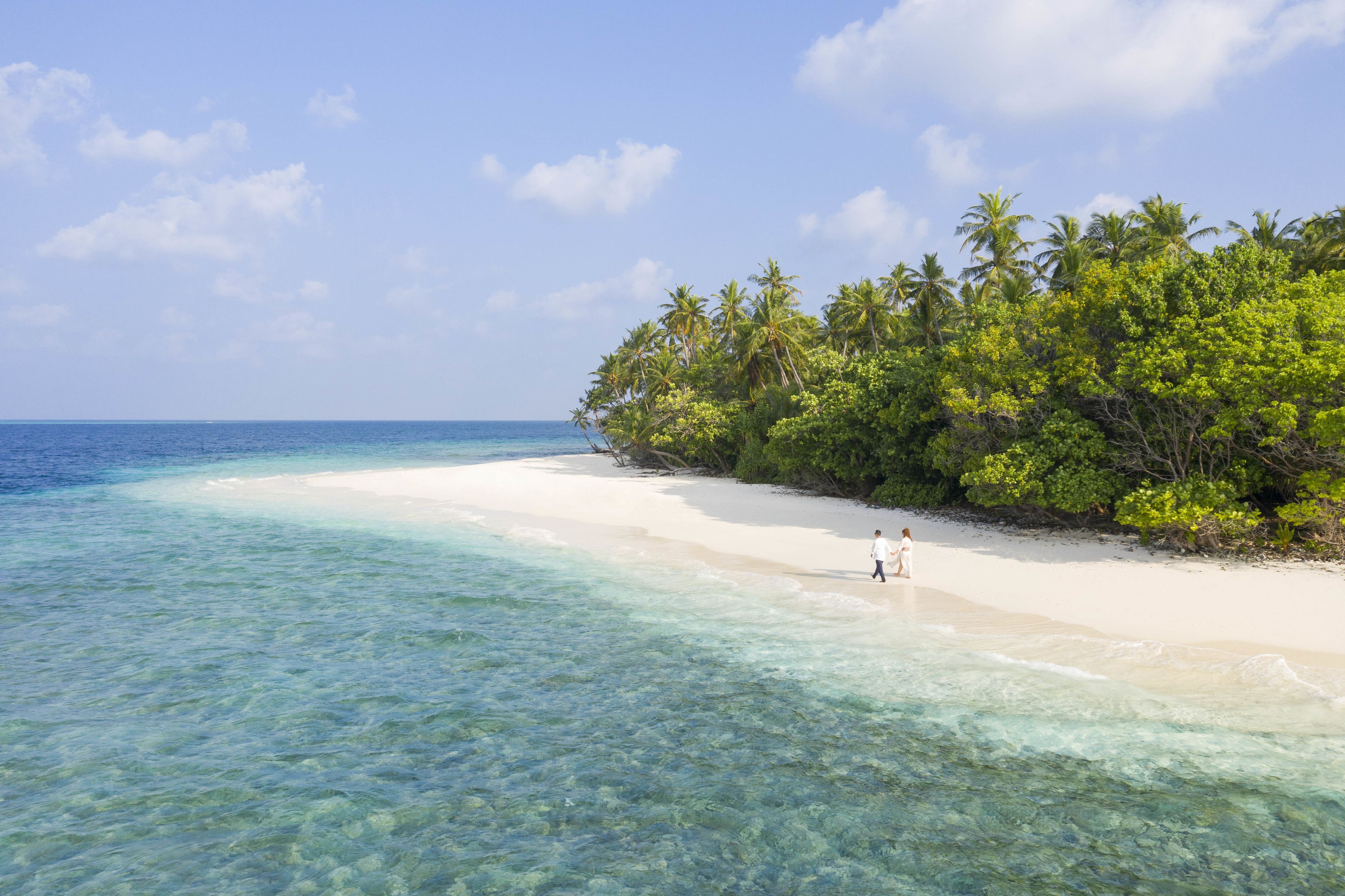 A beach with clear turquoise water, white sand, and lush green vegetation.