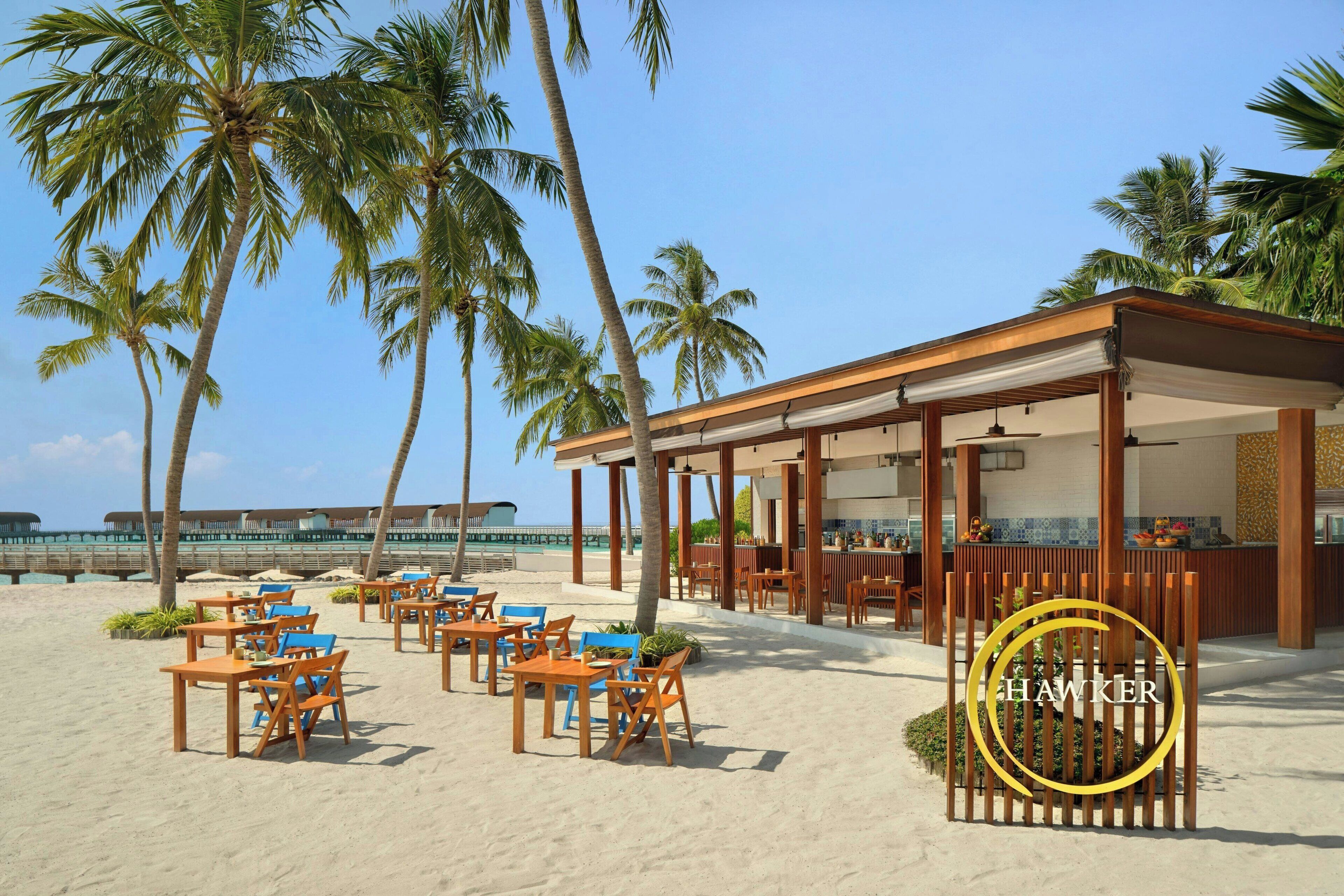 Ein Restaurant direkt am Strand mit Außenbereich, Palmen und Meerblick.