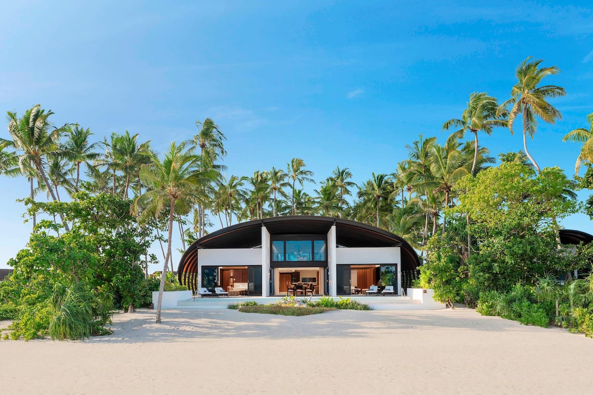 A modern beachfront property with a curved roof, large windows, and a patio area.