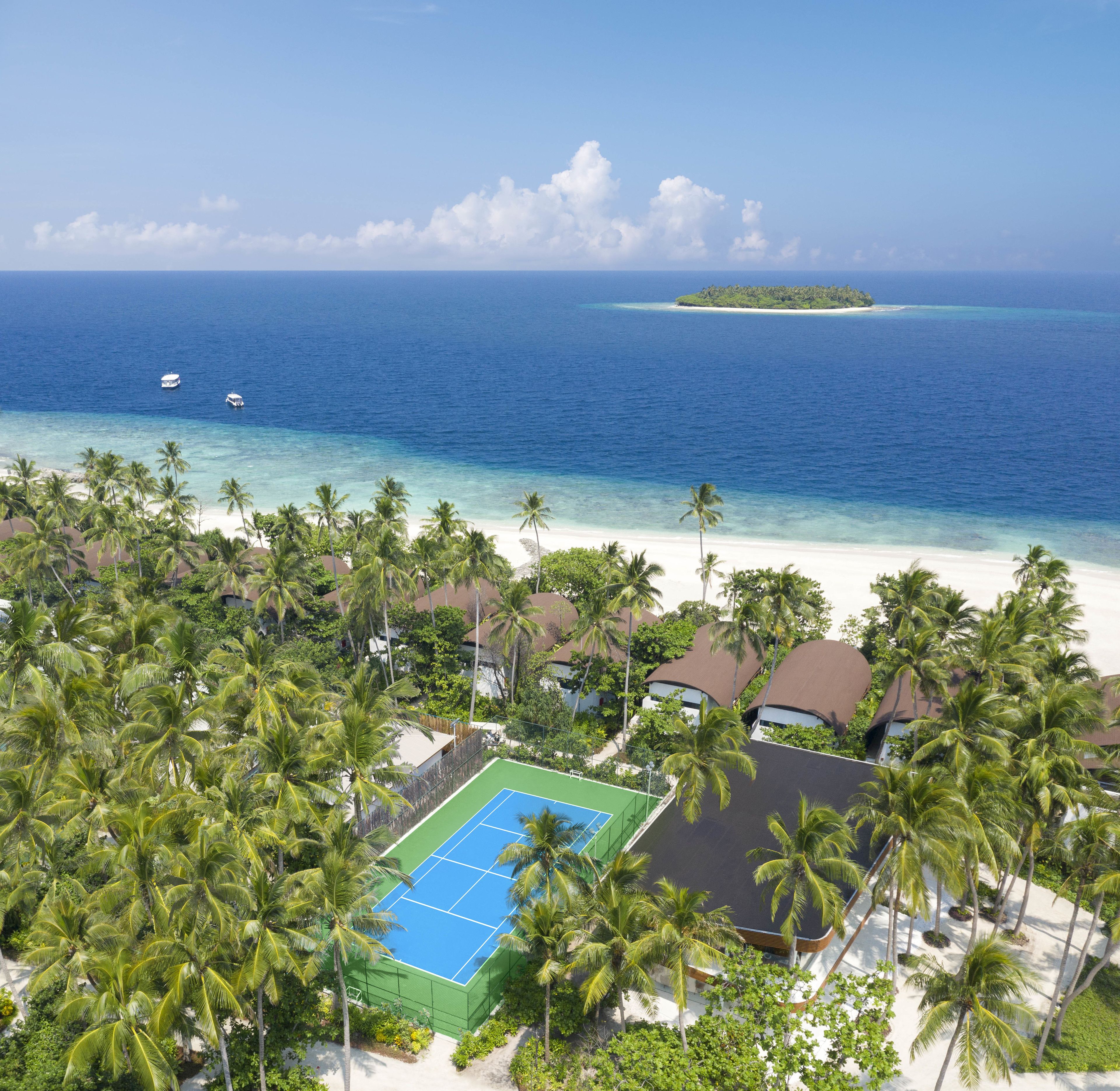 A beachfront property with a tennis court, palm trees, and ocean views.