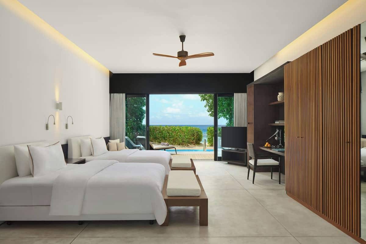 A modern bedroom with two beds, a ceiling fan, and a view of the ocean.