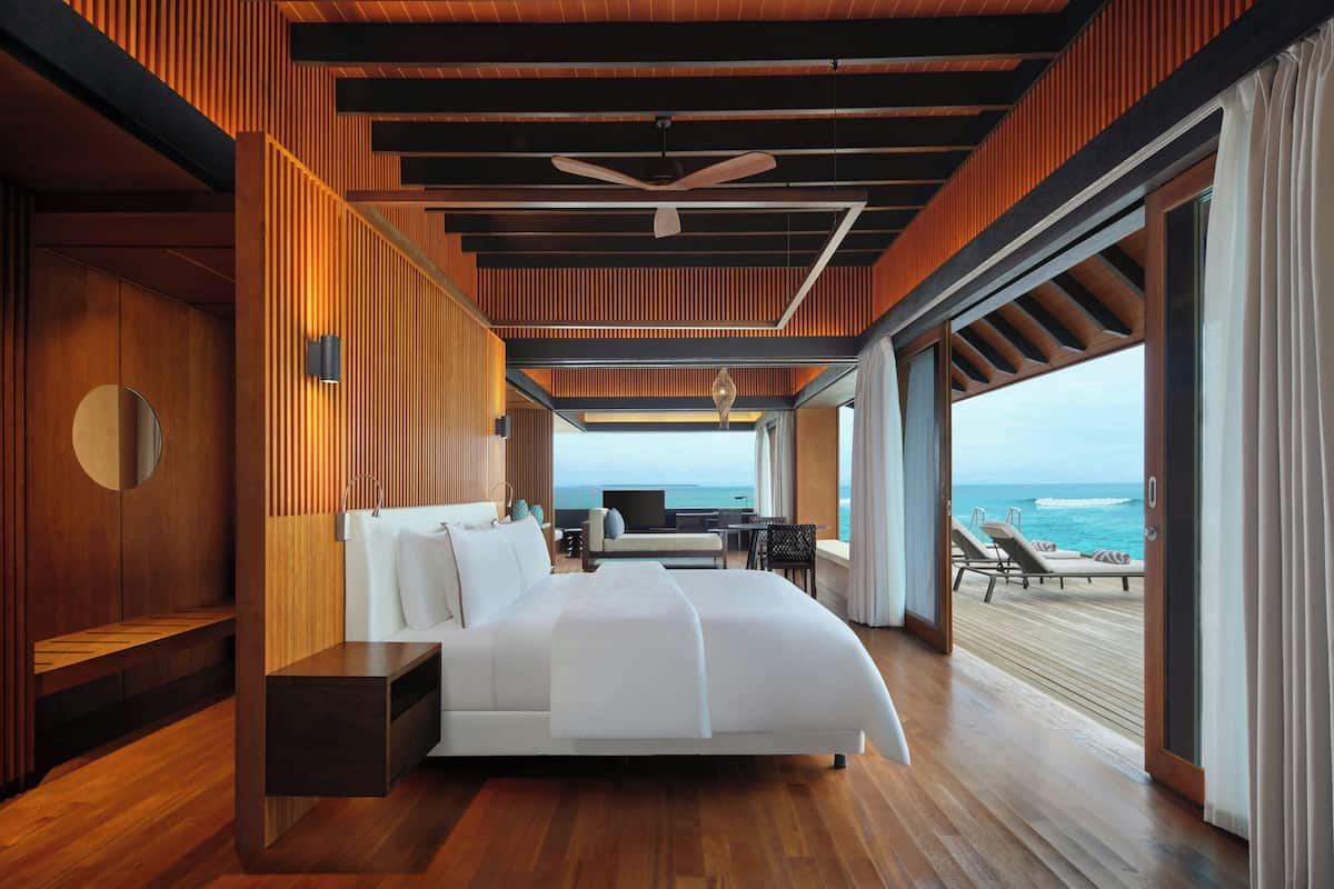 A modern bedroom with a large bed, a desk, and a view of the ocean.