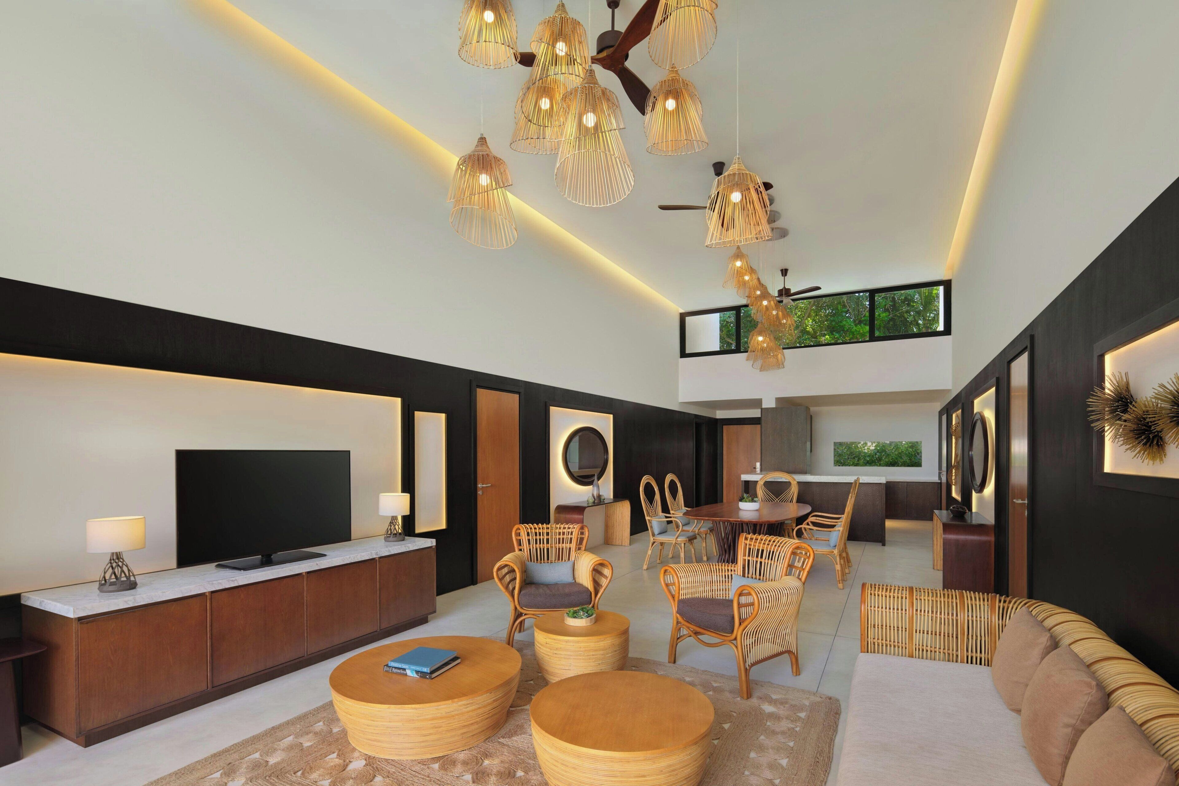 Una sala de estar moderna con televisor de pantalla plana, mobiliario de mimbre y una zona de comedor con techo alto e iluminación colgante.