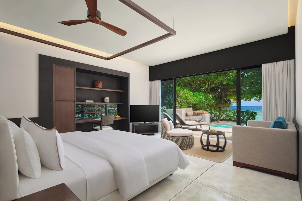 A modern hotel room with a bed, TV, seating area, and a view of the ocean.