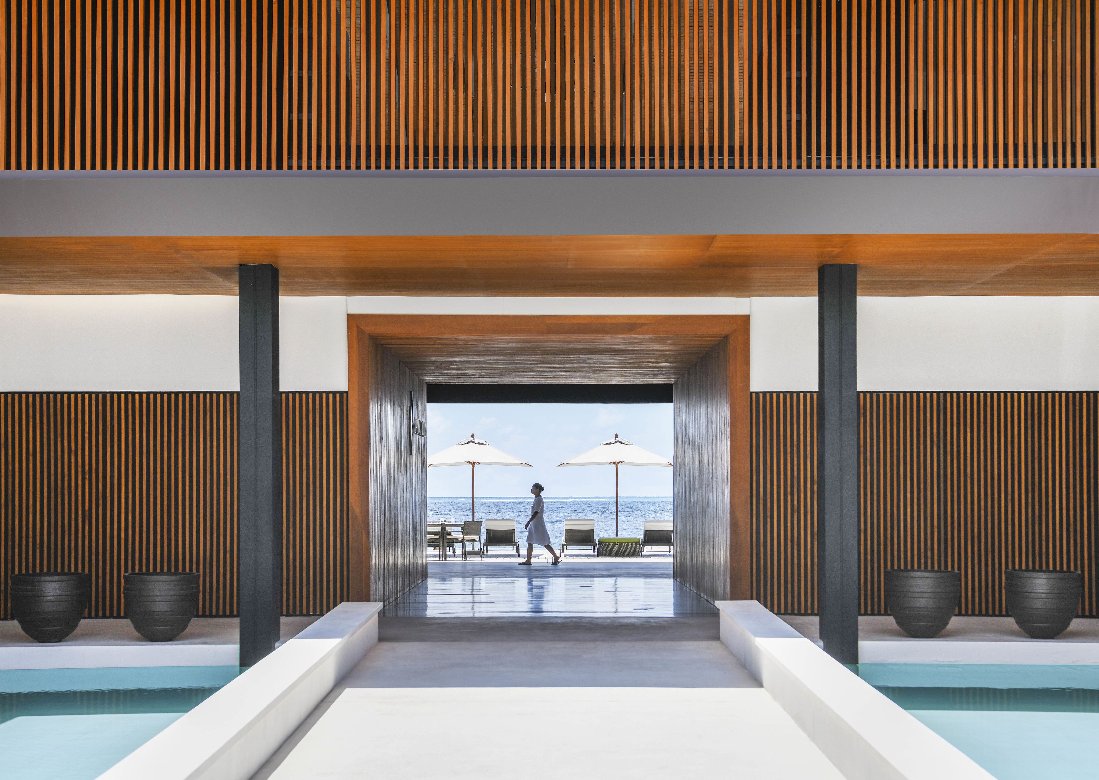 Entrada moderna de un complejo turístico con piscina, paneles de madera y asientos al borde de la piscina.