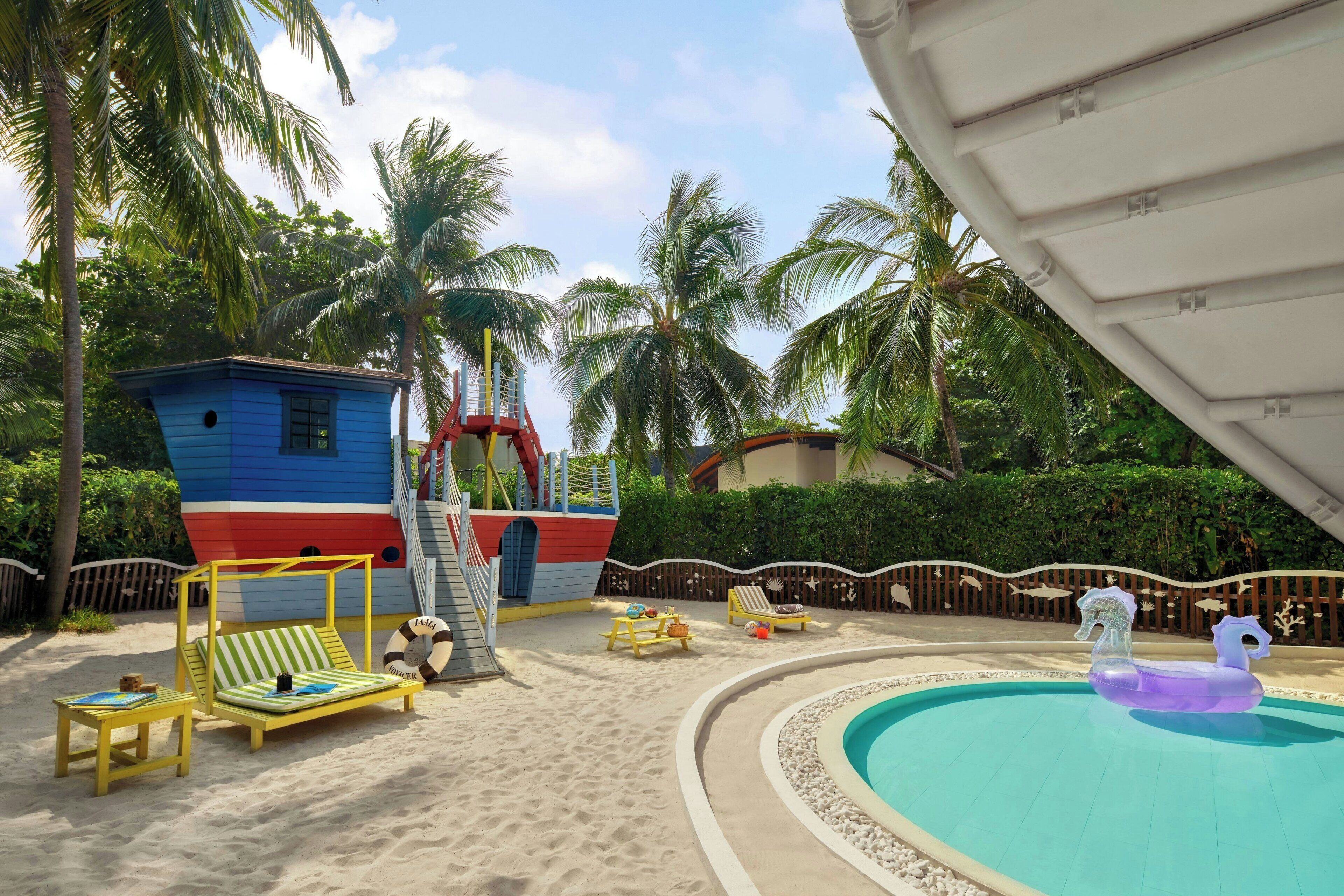 Zona de piscina con una estructura de juego con forma de barco, sillas de descanso y una pequeña piscina con un juguete hinchable morado.