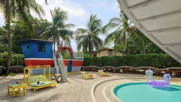 Zona de piscina con una estructura de juego con forma de barco, sillas de descanso y una pequeña piscina con un juguete hinchable morado.