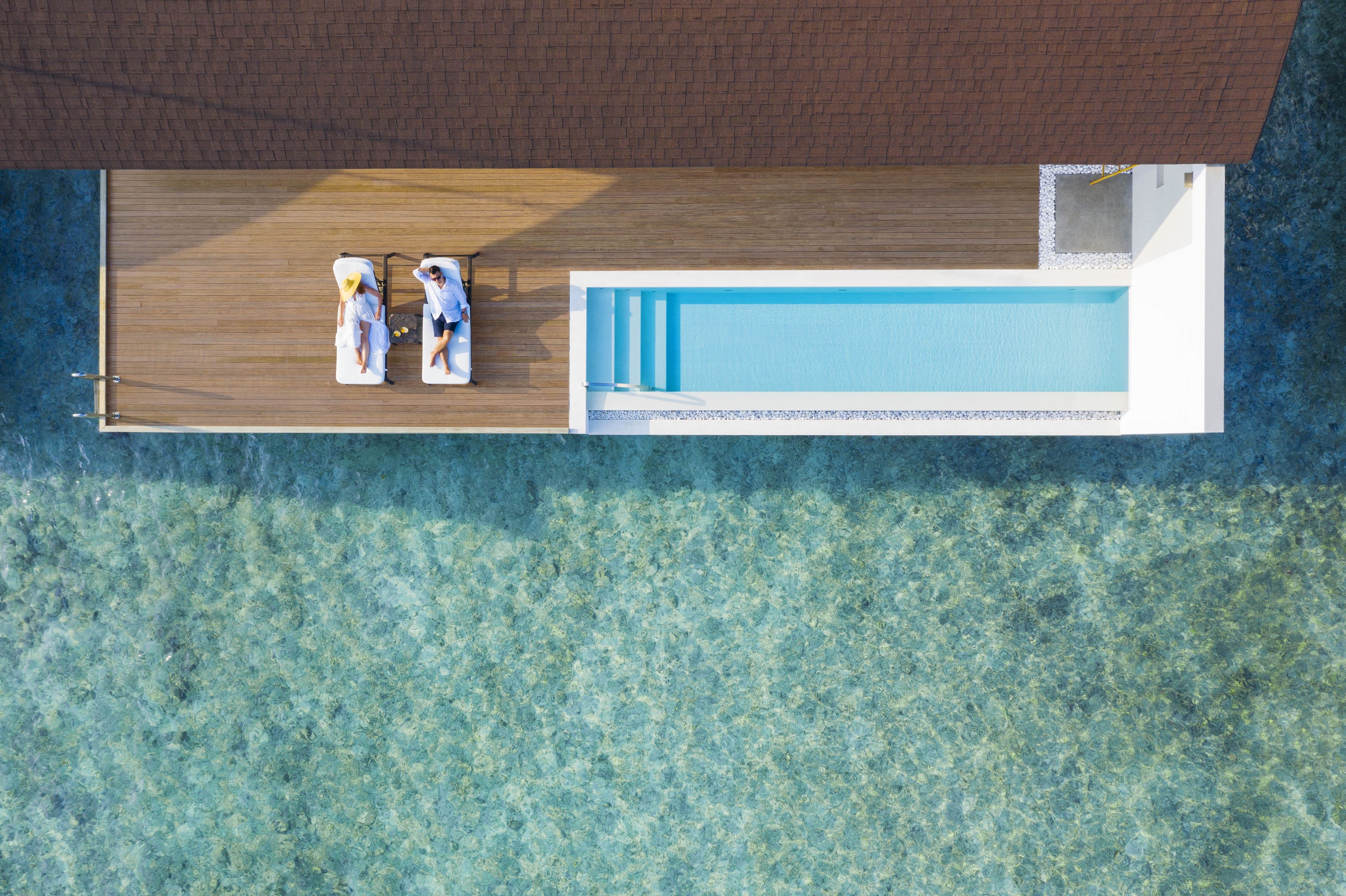 Vista aérea de una piscina moderna con dos sillas de descanso y una terraza de madera.