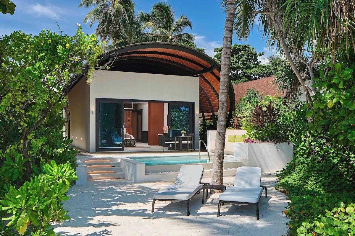 A modern villa with a pool, surrounded by lush greenery and palm trees.