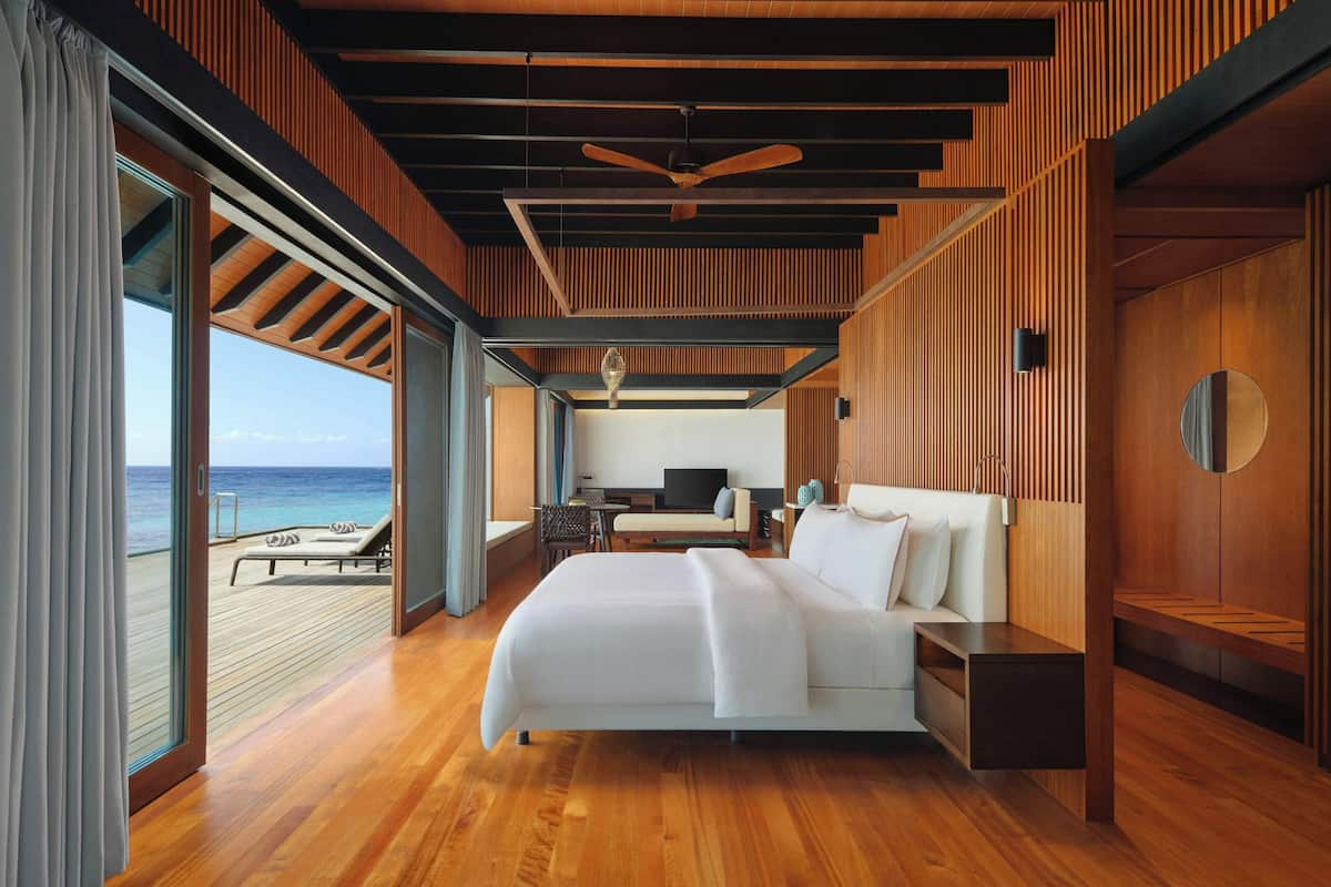 A modern hotel room with a large bed, a TV, a desk, and a view of the ocean.