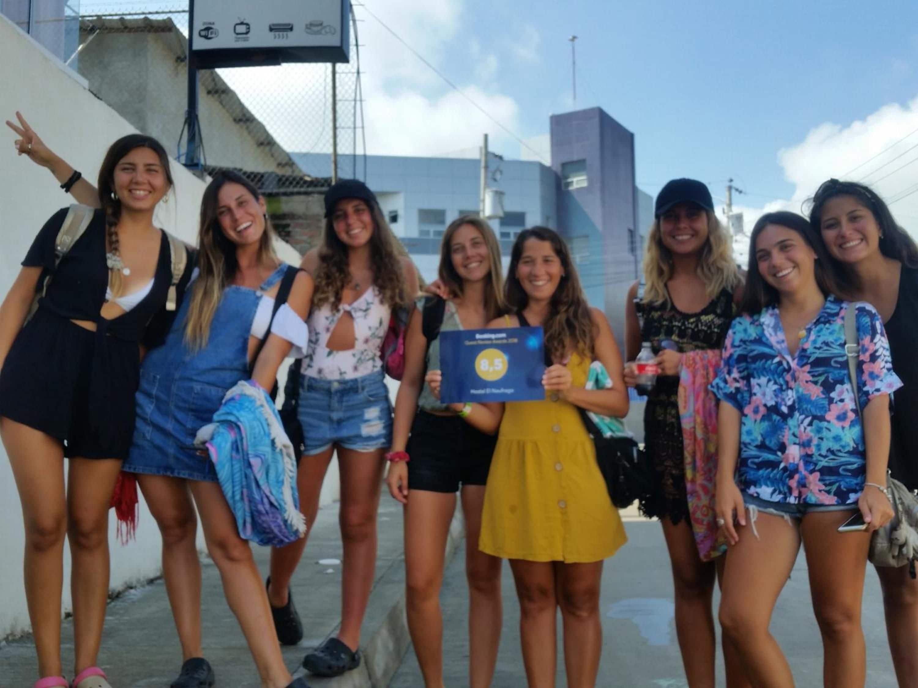 A group of people standing on a sidewalk with a building in the background.