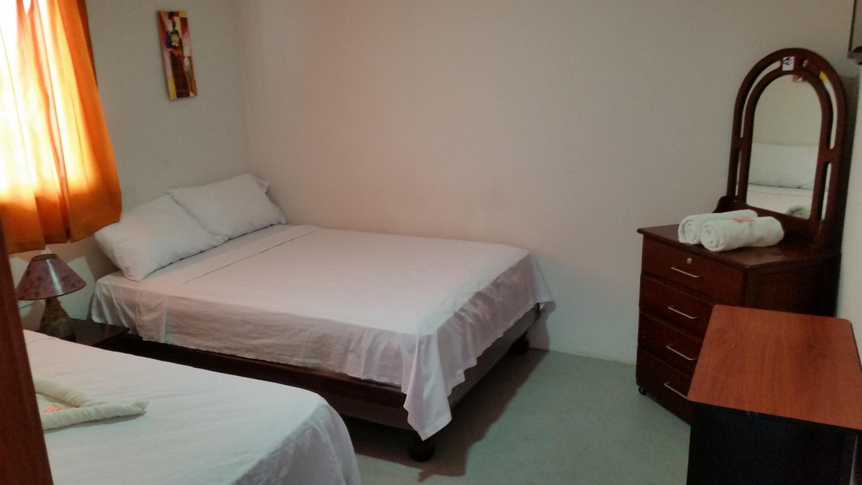 A single-bed room with a wooden dresser, a mirror, and a lamp.