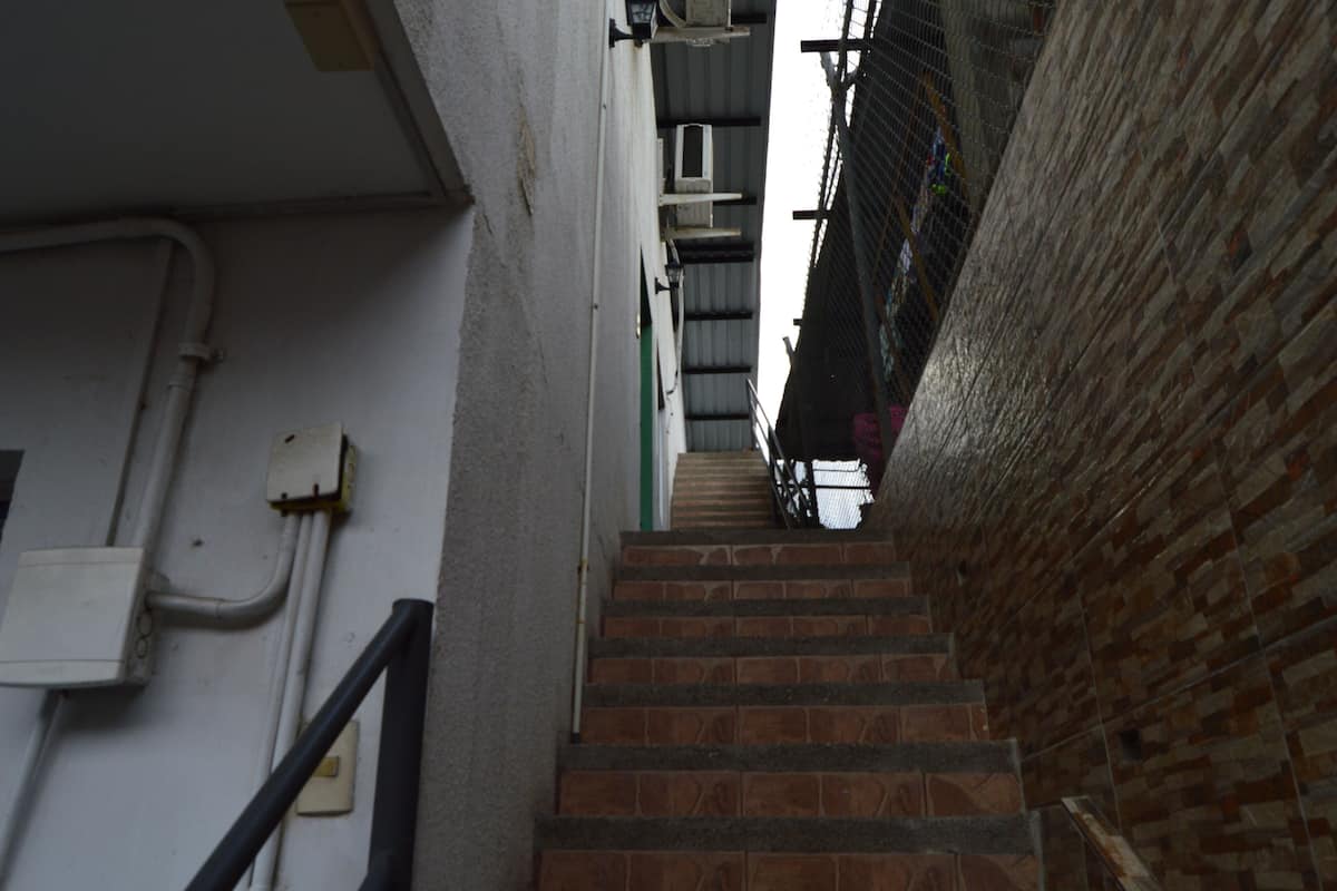 A narrow stairway with a brick wall on one side and a white wall with pipes on the other.