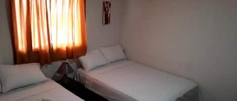 A room with two single beds, a nightstand with a lamp, and a window with curtains.