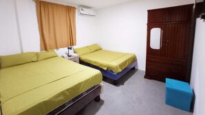 Una habitación con dos camas, un armario de madera, una caja de almacenamiento azul y un equipo de aire acondicionado blanco.