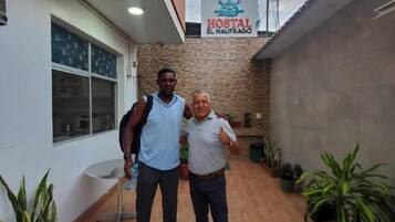 Two individuals standing in a courtyard with a sign for 'Hostal El Naufrago' above.
