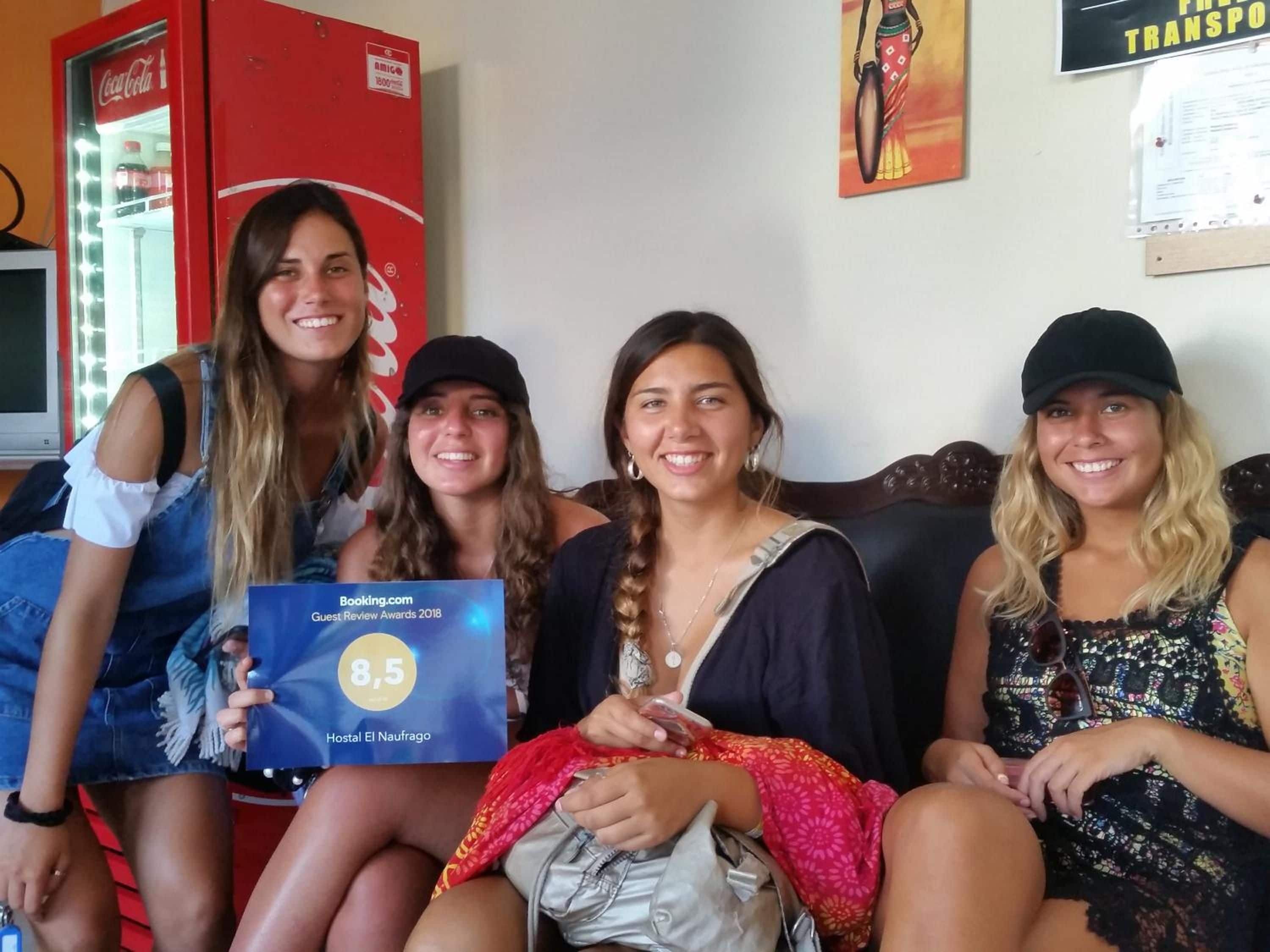 A group of people seated on a couch with a Coca-Cola refrigerator and a wall poster in the background.