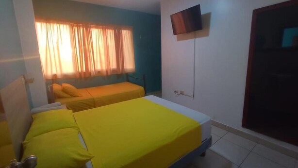 Una habitación con dos camas, televisión montada en la pared y una ventana con cortinas.