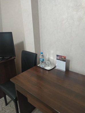 Habitación de hotel con una mesa de madera, una silla, una botella de agua, un vaso y un cartel de menú.