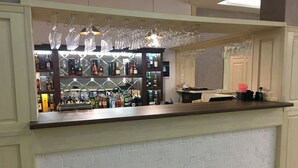A bar area with a white brick wall, shelves stocked with liquor bottles, and hanging wine glasses. - Villa Le Grand (Boryspil)
