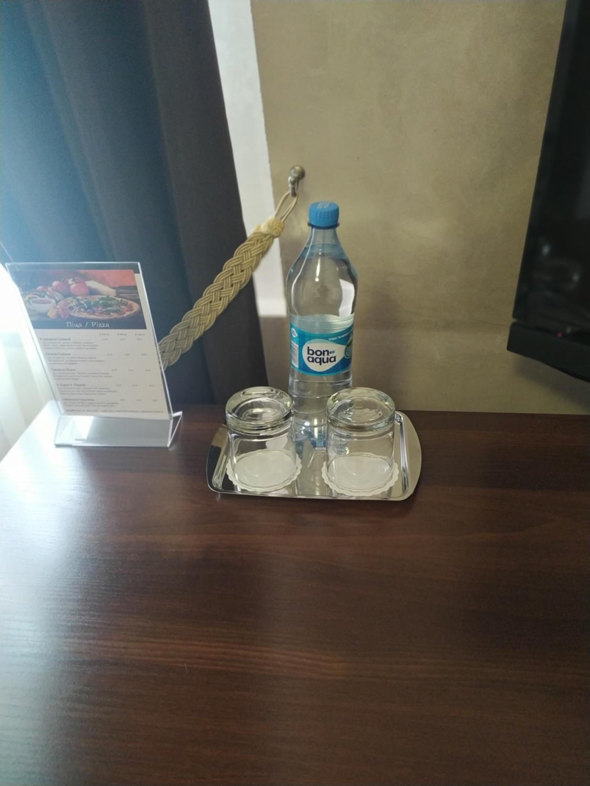 A water bottle, two glasses, and a menu on a wooden table.