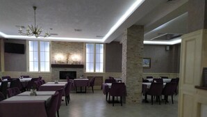 A dining area with tables and chairs, a chandelier, stone pillars, and a fireplace. - Villa Le Grand (Boryspil)