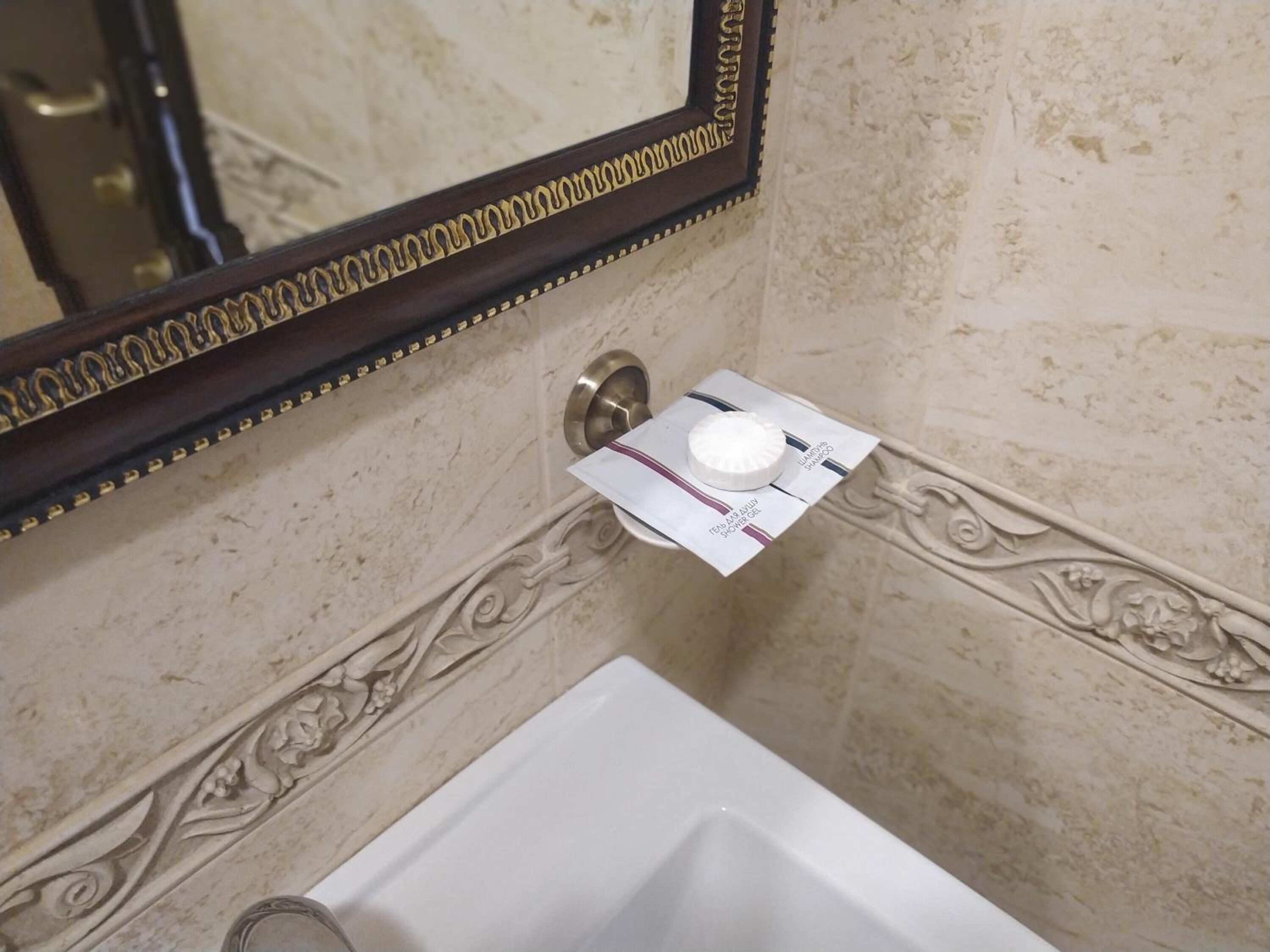 A bathroom with a marble wall, a sink, and a mirror with a decorative frame.