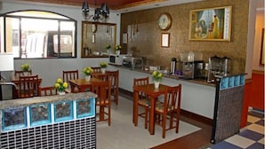 A hotel dining area with wooden tables and chairs, a kitchen counter, and a clock on the wall. - Hotel Parks Vila Mariana (São Paulo)