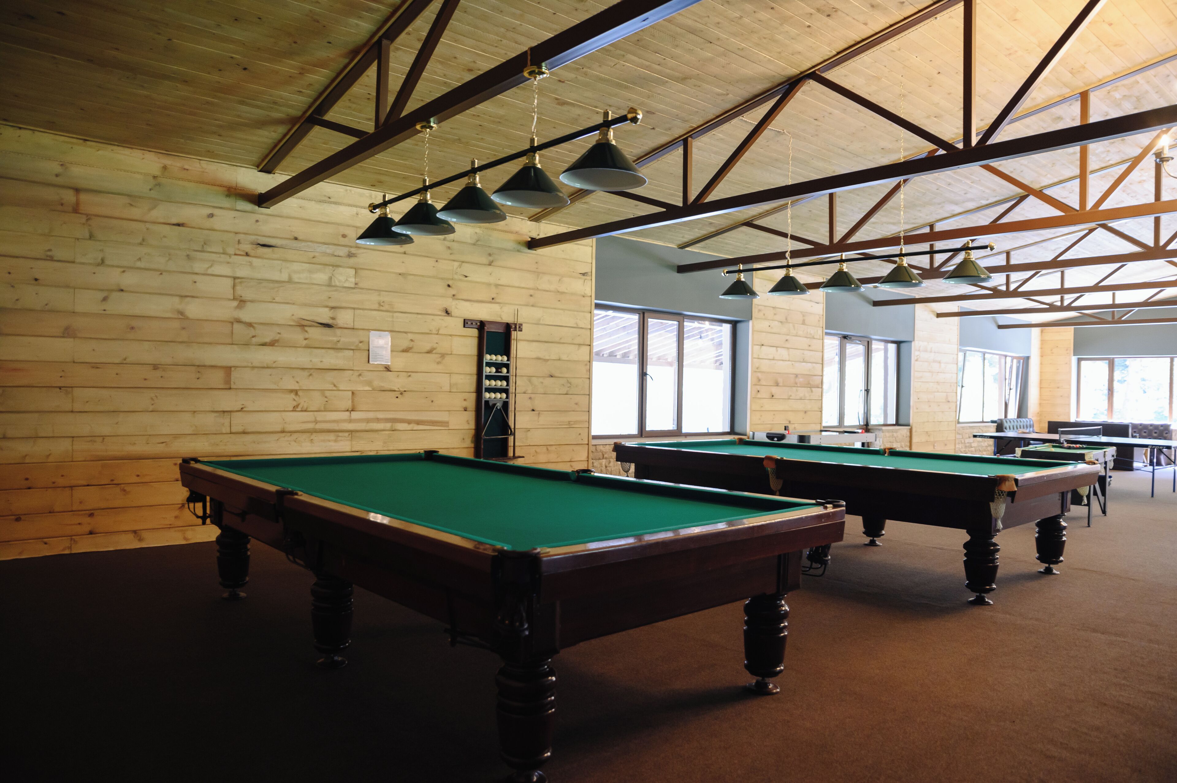 A pool hall with multiple pool tables, wooden walls, and hanging lights.