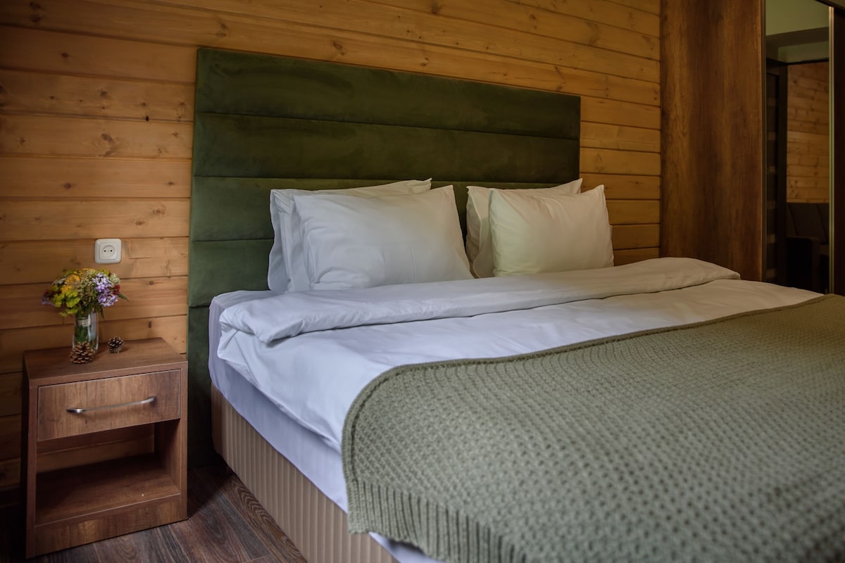 A wooden-paneled room with a bed, a nightstand with a vase of flowers, and a green headboard.