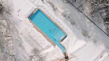 Vista aérea de una piscina rectangular rodeada de nieve, con algunas personas nadando.