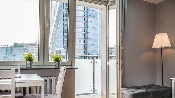 A modern living room with a balcony, a dining area, and a grey sofa. - 55 Plater Residence (Warsaw)