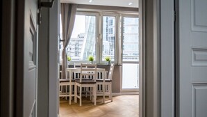 An open doorway leading to a dining area with a wooden floor, a table with chairs, and large windows with curtains. - 55 Plater Residence (Warsaw)