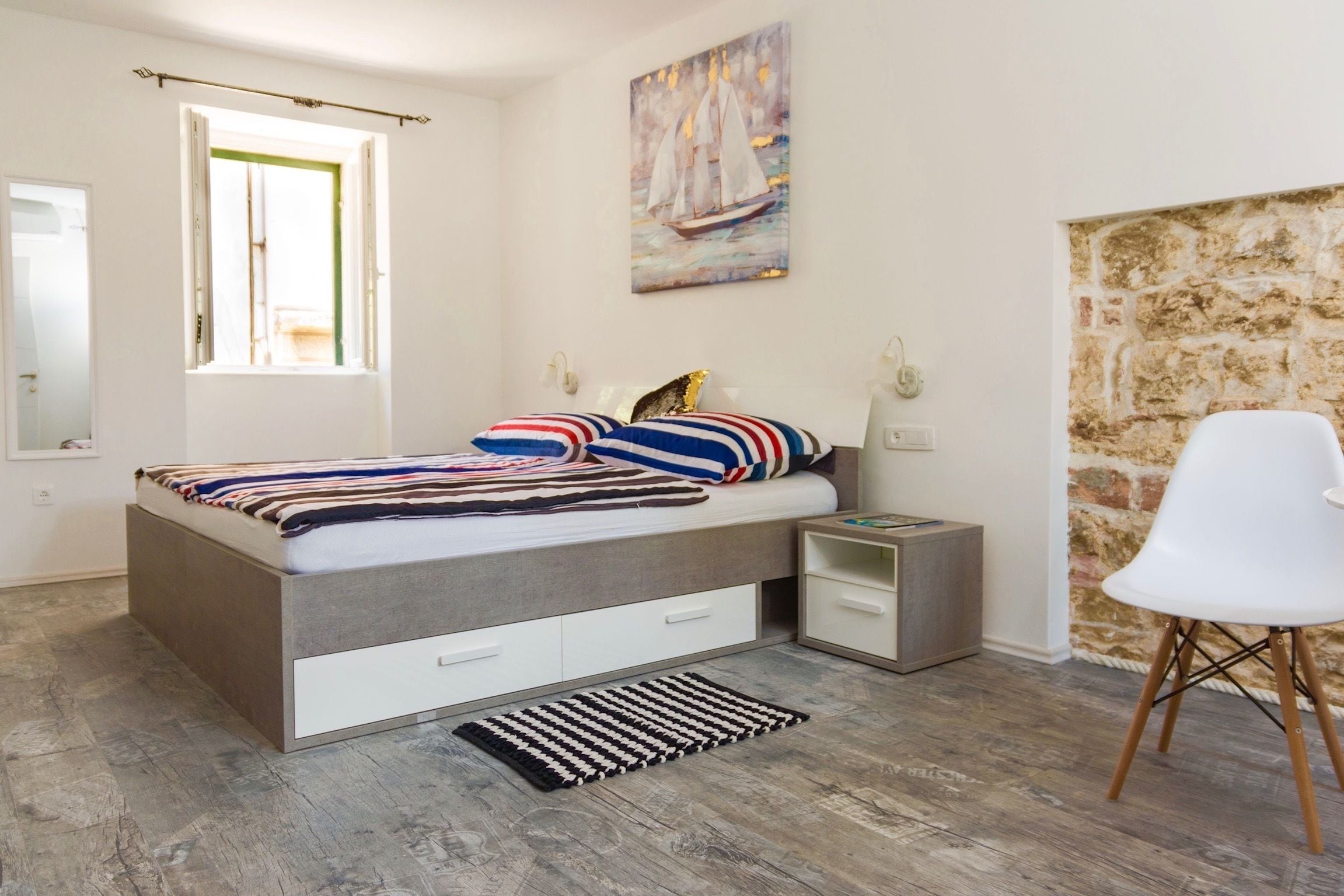 Una camera da letto con un letto, comodini, una sedia, una finestra, un quadro e una parete in pietra.