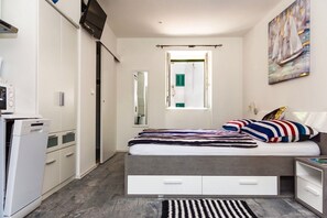 A modern bedroom with a bed, bedside tables, a wardrobe, a built-in TV, and a window with a view of the bathroom. - Villa Minerva Gardens (Split)