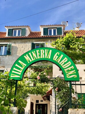 Villa Minerva Gardens entrance with a sign, a building with green shutters, and a tiled roof. - Villa Minerva Gardens (Split)