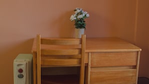 Un escritorio de madera con cajones, una silla, una pequeña planta en maceta, un televisor montado en la pared y un electrodoméstico blanco en el suelo.