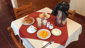 Una mesa de desayuno con cruasanes, fruta, huevos y una cafetera.