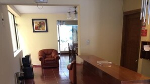 Un área de recepción con mostrador de madera, alfombra estampada, sofá de cuero marrón y un cuadro en la pared.