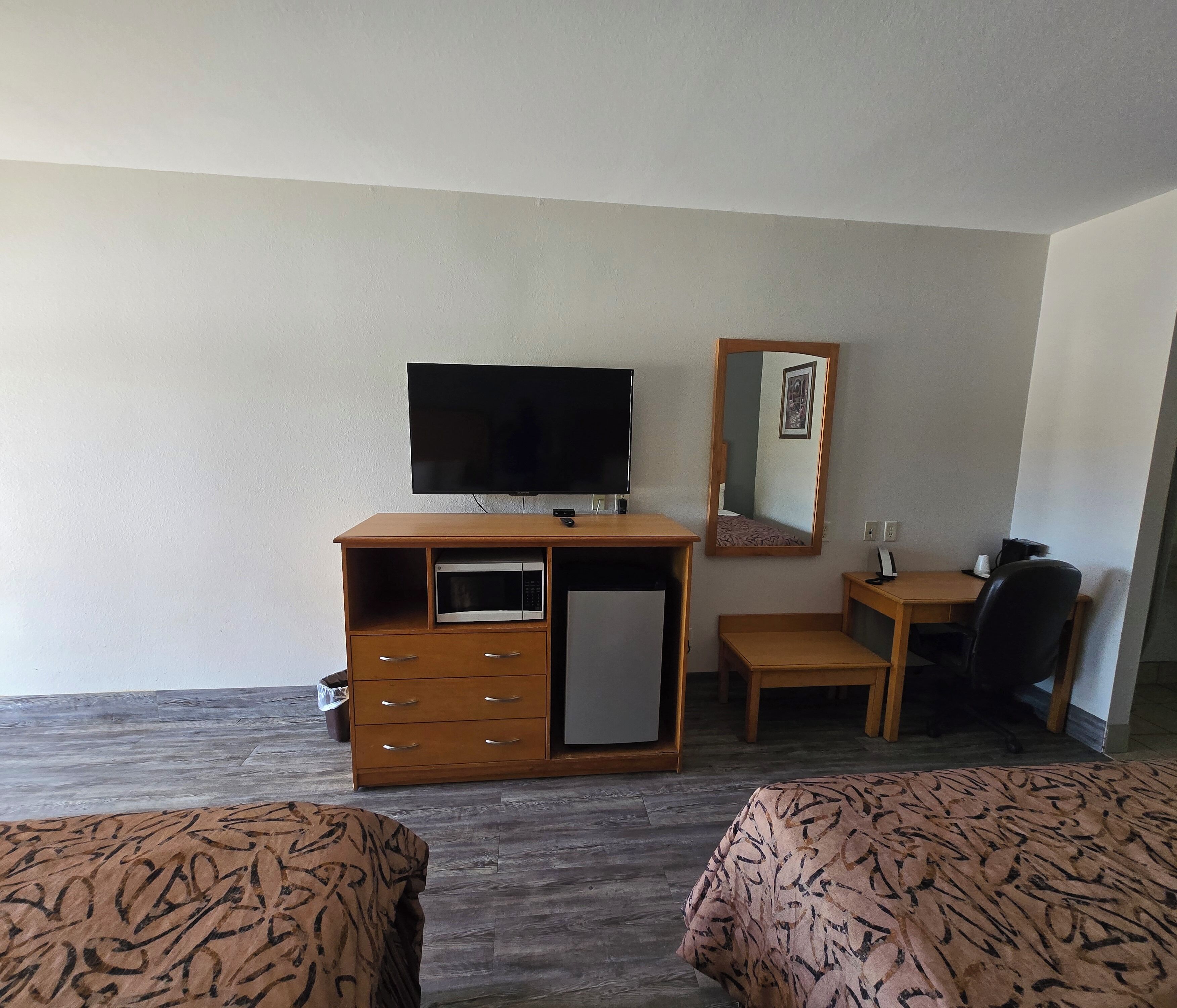 Quarto de hotel com escrivaninha de madeira, televisão, micro-ondas, mesa pequena, cadeira e duas camas.