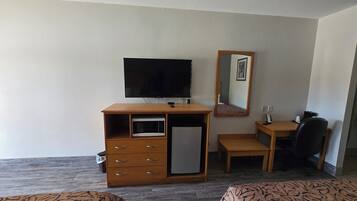 Quarto de hotel com escrivaninha de madeira, televisão, micro-ondas, mesa pequena, cadeira e duas camas.