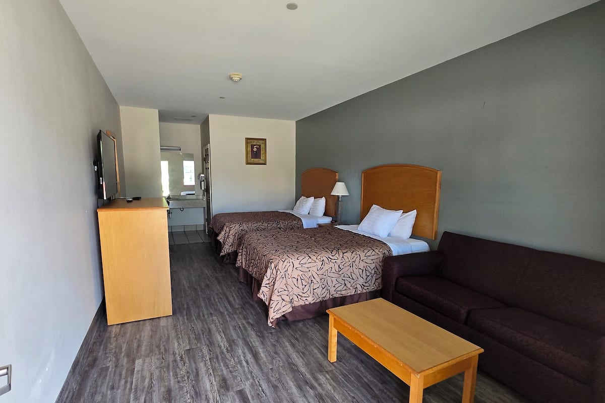 A hotel room with two beds, a wooden desk, a sofa, and a television on a stand.