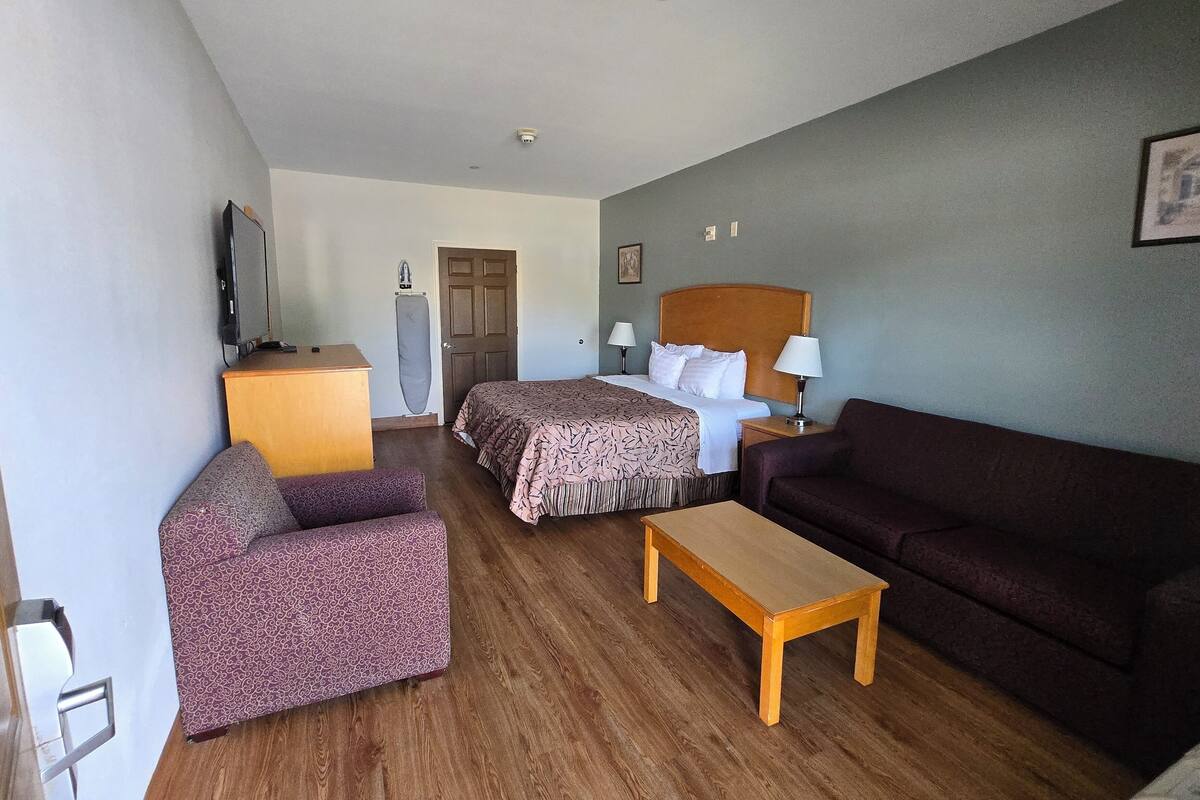 A hotel room with two beds, a sofa, a small table, a TV, and a door.