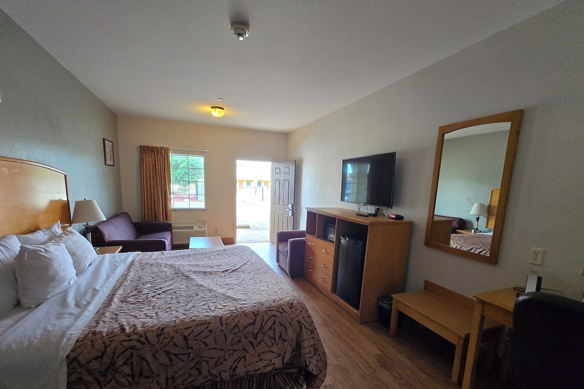 A hotel room with a large bed, a desk, a television, and a mirror.